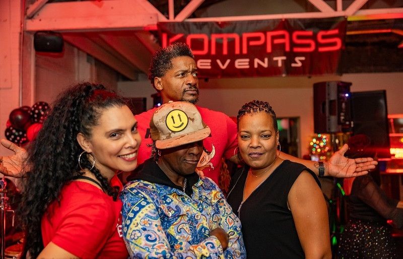 Group of four people posing at an event, with a Kompass Events banner in the background.