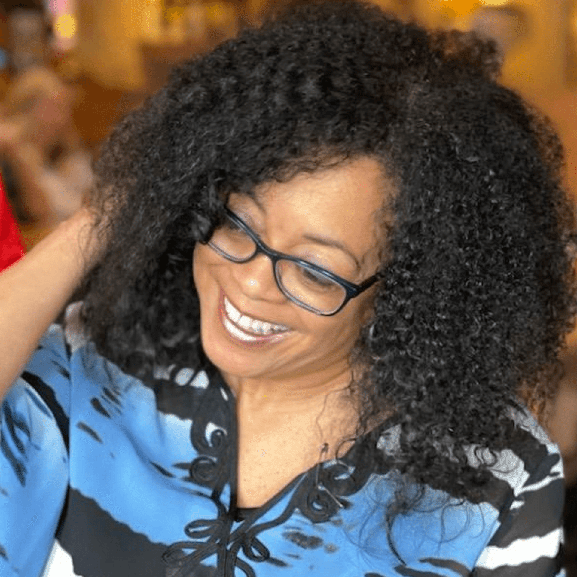 Person wearing a blue and black patterned top with curly hair, seen indoors.