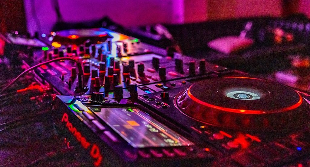 Close-up of a DJ mixing console with illuminated controls and buttons in a dimly lit setting.