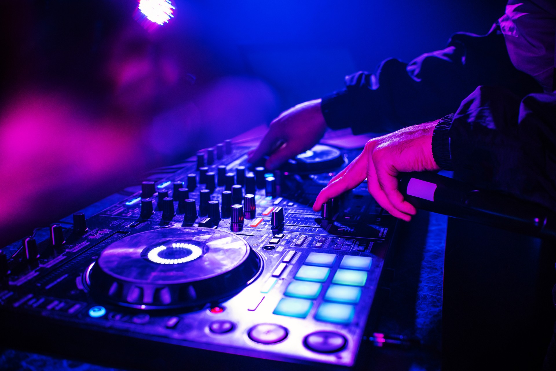 DJ console for mixing music with hands and with blurred people dancing at a night club party