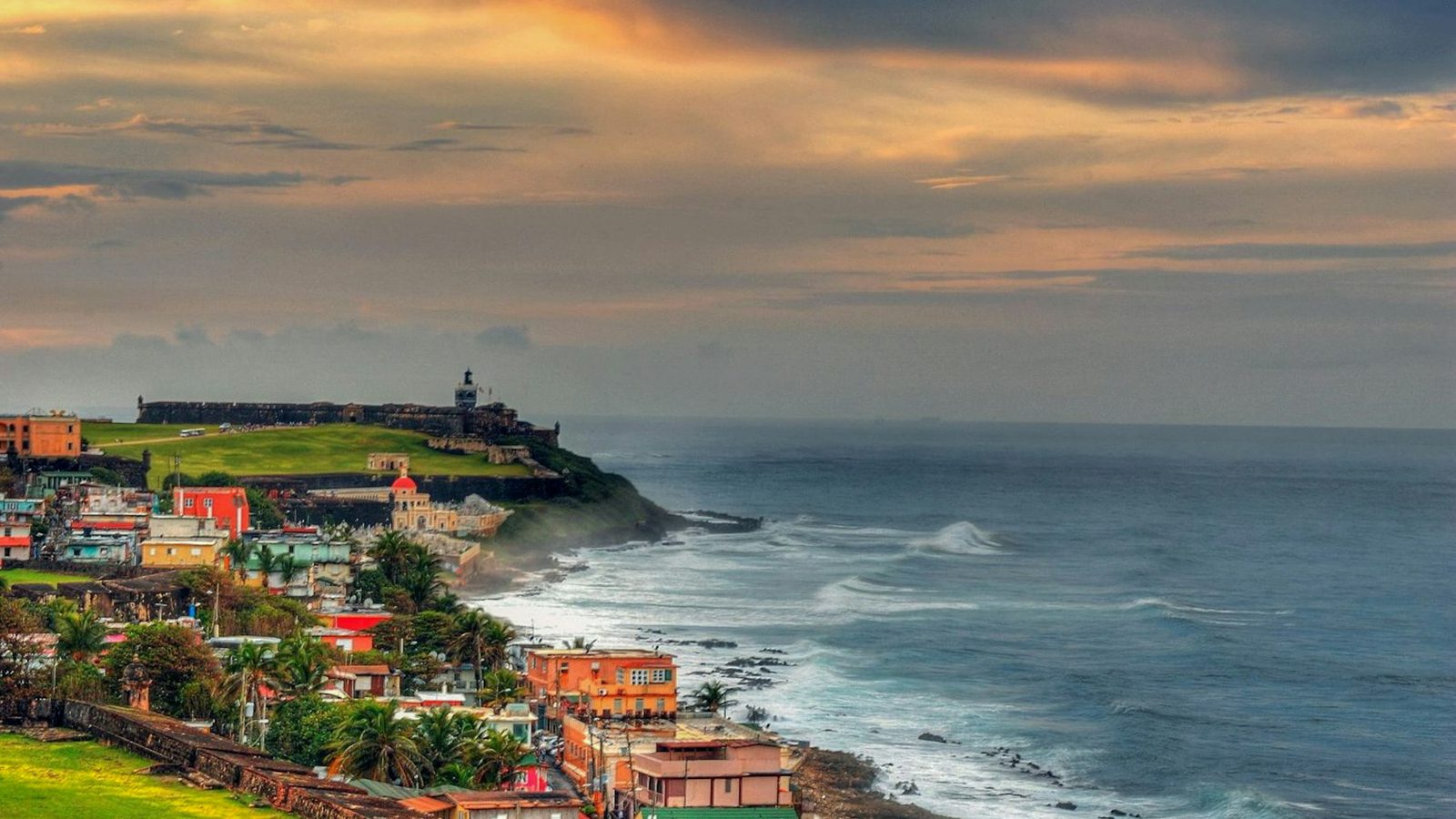 Colorful buildings along the rocky San Juan coastline under a bright sky.