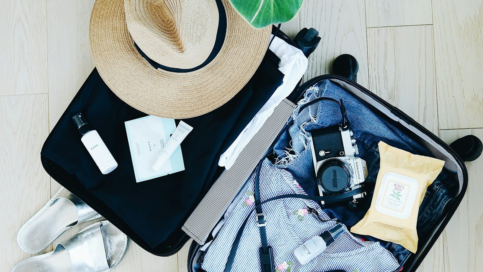 Hands packing a suitcase with rolled clothes, a passport, a camera, and headphones.